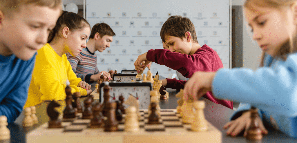 Students playing chess with supportive parents and teachers in the background