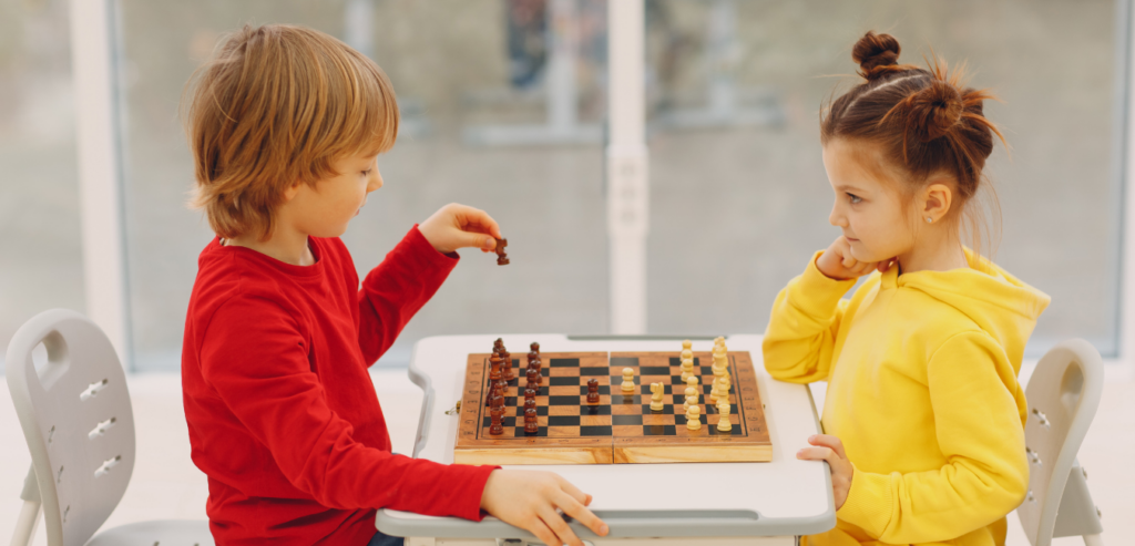 Children playing chess in a classroom with a coach guiding them, illustrating the development of critical thinking skills.